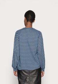 Long-sleeve blue blouse with a geometric pattern. The fabric appears lightweight and textured, paired with a black leather skirt.