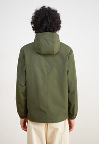 Olivengrüne, leichte Jacke mit Kapuze. Sie verfügt über elastische Bündchen und ein einfaches Design, hergestellt aus glattem, wasserabweisendem Material.