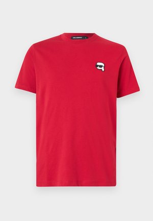 Red cotton T-shirt with a crew neck, featuring a small black and white cartoon face logo on the left chest. Short sleeves, regular fit.