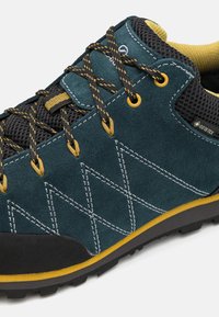 Chaussure de randonnée en daim turquoise foncé avec mesh noir, accents jaunes et semelle en caoutchouc. Présente des coutures en zigzag et des lacets ronds.