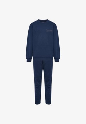 To børn stående side om side iført matchende marineblå sweatshirts, bukser og blå sneakers på en helt hvid baggrund.