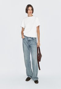 T-shirt bianco a maniche corte abbinato a jeans a gamba larga blu chiaro. Completa l'outfit con scarpe in pelle marroni e una borsa a tracolla marrone.