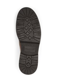 Semelle de chaussure en caoutchouc noir avec un motif de texture, présentant diverses formes et une étiquette du fabricant "Marc O'Polo" avec la taille 42.