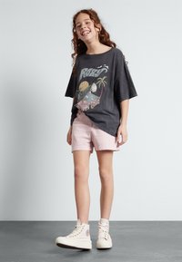 Grå grafisk T-shirt med tropisk design, ljusrosa shorts och vita högtoppsneakers. Släta texturer, avslappnad passform och avslappnad stil.
