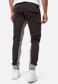 Cargo-Hosen aus schwarzem Hauptstoff, grauen Seitenteilen und gerippten Bündchen. Verfügt über Taschen und eine lockere Passform. Kombiniert mit weißen Sneakern.