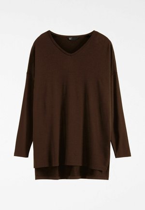 Brūns garām piedurknēm V veida kakla tops no mīkstas auduma. Ļoti vaļīgs piegriezums ar sānu šķēlumiem, garums līdz gurniem. Bez rakstiem vai rotājošiem elementiem.