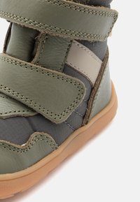 Grüne Leder- und Textilstiefel mit Klettverschlüssen, gepolstertem Schaft, grauen Akzenten und Gummisohle. Strukturiertes Finish mit sichtbaren Nähten.