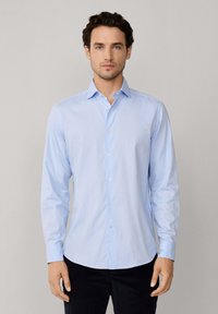 Camisa de botones de manga larga color azul claro, hecha de una tela suave, con un cuello puntiagudo, dobladillo recto y una tapeta abotonada.
