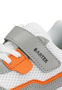Primo piano di una sneaker bianca e grigia con accenti arancioni, caratterizzata da lacci bianchi e una fascia in velcro grigia etichettata "BARTEX."