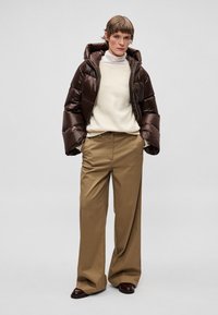 Pruun kapuutsiga sulejope, hele beež kardigan ja laiad kahvlikroogi püksid. Jopel on läikiv tekstuur ja tõmblukuga sulgemine.