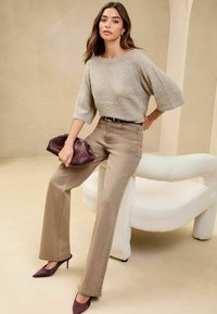 Beige zkrácený svetr s texturovaným pletením; kalhoty s vysokým pasem v světle hnědé barvě a širokém střihu; tmavě fialová tkaná kabelka; špičaté podpatky.