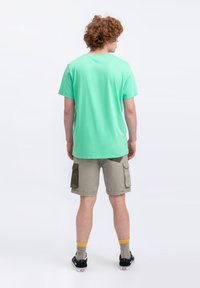 T-shirt in cotone verde menta con maniche corte, abbinato a pantaloni cargo beige con due tasche laterali e accenti verdi a contrasto.