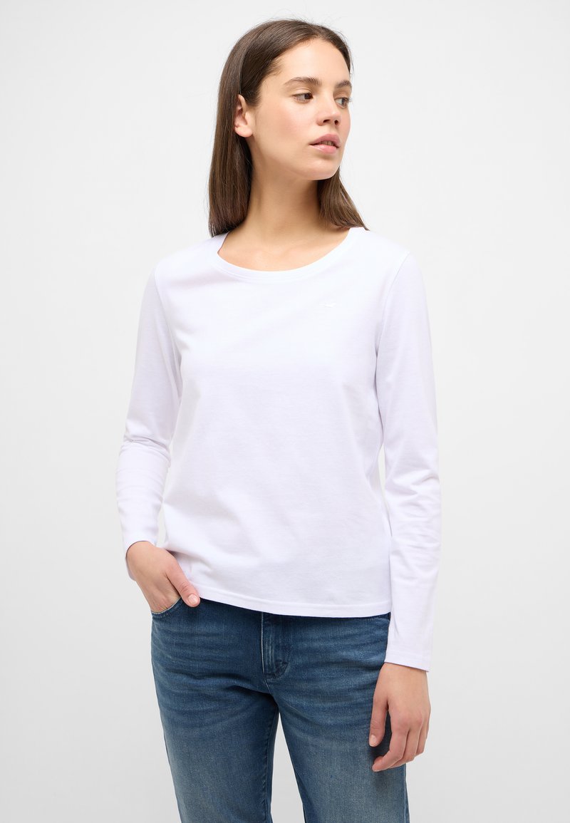 Weißes Langarm-T-Shirt aus weicher Baumwolle mit rundem Halsausschnitt. Verfügt über ein kleines Logo auf der Brust und einen lockeren Schnitt. Getragen mit blauen Jeans.