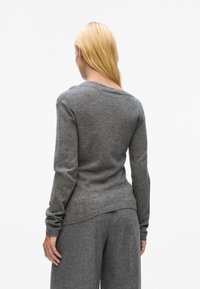 Gray, long-sleeve sweater made of soft fabric, featuring a round neckline and a relaxed fit. The back hem is slightly longer than the front.