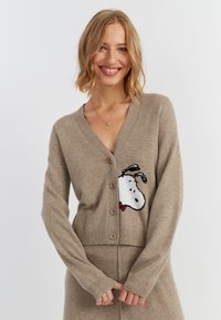 Cardigan a maglia beige con un design ricamato di Snoopy sul lato sinistro del petto, con scollatura a V e cinque bottoni sulla parte anteriore.