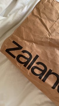 Bolsa de papel marrón arrugada con texto negro grande parcial "Nala" sobre una superficie de tela blanca.