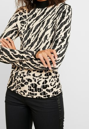 Top aderente a maniche lunghe in un motivo geometrico beige e nero, con un colletto alto a costine e un tessuto testurizzato. Abbinato a pantaloni neri.