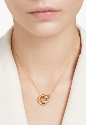 Gouden ketting met twee in elkaar verstrengelde ringen, waarvan er één gepolijst is en de ander bezet met heldere kristallen, hangend aan een verfijnde ketting.