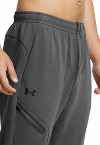 Gray athletic pants with elastic waistband, side pockets, and a zippered pocket. Made from soft material with a smooth texture.