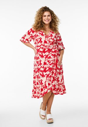 Rotes und cremefarbenes Blümchen-Wickelkleid mit kurzen Ärmeln, knielangem Saum und einer Bindegürteldetail. Kombiniert mit weißen Plateausandalen.
