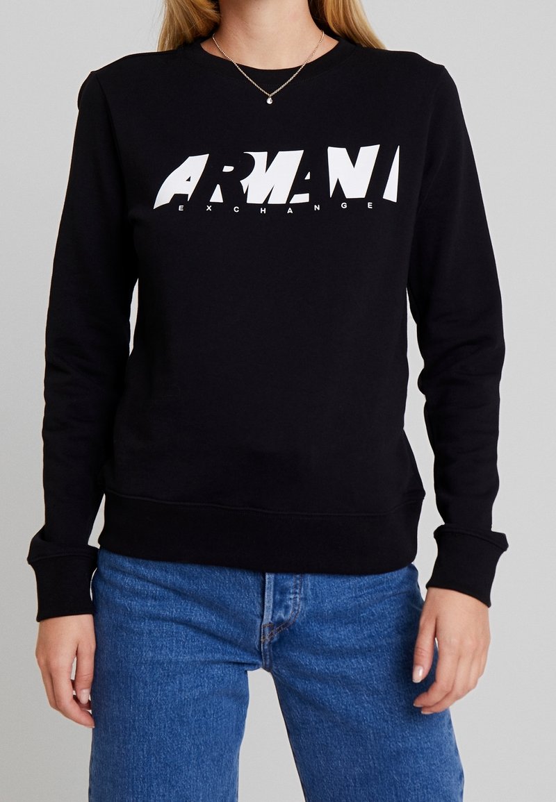 Svart sweatshirt i bomullsblandning, med en vit logotyp fram med stiliserad text. Långärmad med ribbade muddar och fåll.