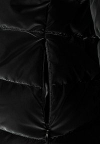 Sort dunjakkeafsnit med en lynlåsåbning. Glat tekstur med quiltet mønster og subtil glans på stoffet.