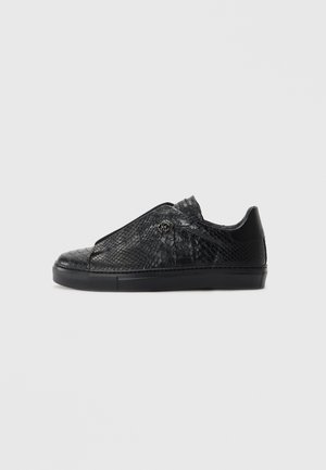 Baskets basses en cuir noir avec un motif de serpent texturé et semelle en caoutchouc noire, vue de côté sur fond blanc.