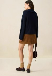 Marineblauw geribbelde sweater, bruin suède rok, bruine gebreide sokken, burgundy schoenen, kleine handtas. Minimalistisch ontwerp met textuurvariaties.