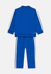 Blauw trainingspak bestaande uit een ritssluitingsjasje met witte zijkanten en bijpassende broek. Gemaakt van gladde stof met geribbelde manchetten en kraag.