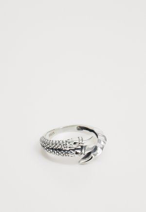 Ezüst gyűrű, amelyen karomra emlékeztető dizájn látható, textúrázott pikkelyekkel, sima felülettel és S925 jelöléssel, egy lény végtagjára hasonlít.