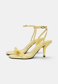 Gelbe Lackleder-Sandaletten mit dünnen Knöchelriemen, quadratischen Zehen und 7,5 cm hohen Stilettos, die schwarze Absatzspitzenakzente aufweisen.