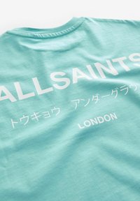 Turkos bomullströja med stor vit text som säger "ALLSAINTS" och "LONDON", samt ytterligare text på olika språk.
