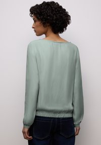 Blouse vert menthe à manches longues en tissu léger avec un large décolleté et un ourlet élastiqué, associée à un jean foncé.