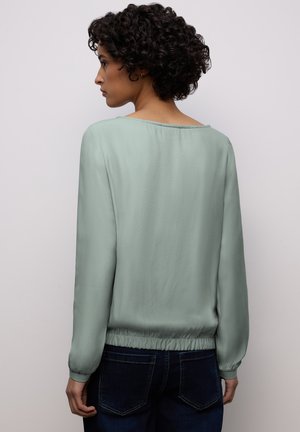 Blouse vert menthe à manches longues en tissu léger avec un large décolleté et un ourlet élastiqué, associée à un jean foncé.