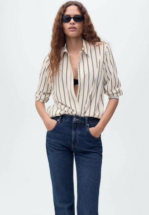 Gestreiftes Hemd in Creme und Marineblau, vorne aufgeknöpft, kombiniert mit dunkelblauen Jeans. Das Model hat lange, wellige Haare und trägt schwarze Sonnenbrillen.