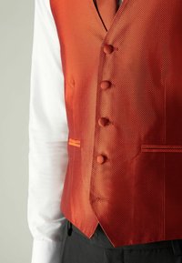 Gilet orange texturé avec une finition lisse, doté de cinq boutons et d'une poche latérale, porté sur une chemise blanche.
