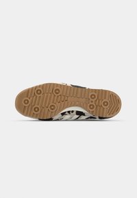 Sneaker with a black and white cow print upper, featuring a textured beige rubber sole with grip patterns and three white stripes.