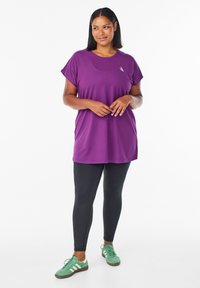 Lilla tunika med korte ærmer, blødt stof, afslappet pasform. Kombineret med sorte leggings og grønne sneakers med hvide detaljer.