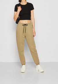 Černý krátký rukávový crop top spárovaný s béžovými tapered tepláky s páskem na stažení. Bílé tenisky dotvářejí outfit.