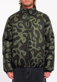 Pufferjack in zwart met groen abstract patroon, rits sluiting, hoge kraag, elastische manchetten en zoom, met een logo patch op de borst.
