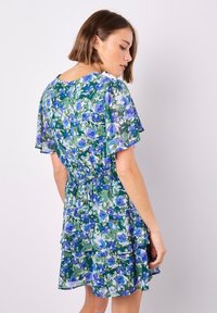 Blumenkleid mit grünem Grund, blauen und lila Blumen, kurzen schwingenden Ärmeln, gesmokter Taille und mehrlagigem Rüschensaum.
