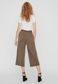 Široké hnědé kalhoty culottes s opaskem v pase, kombinované s přiléhavým bílým tričkem a černými sandály na podpatku. Hladká textura, délka ke kotníkům.