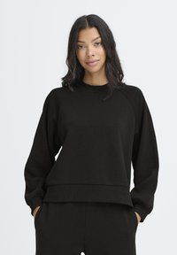 Melnā džemperī ar apaļu kakla izgriezumu, raglānu piedurknēm un brīvu piegriezumu. Iezīmēts ar apstrādātu apakšmalu un mīkstu, strukturētu audumu.