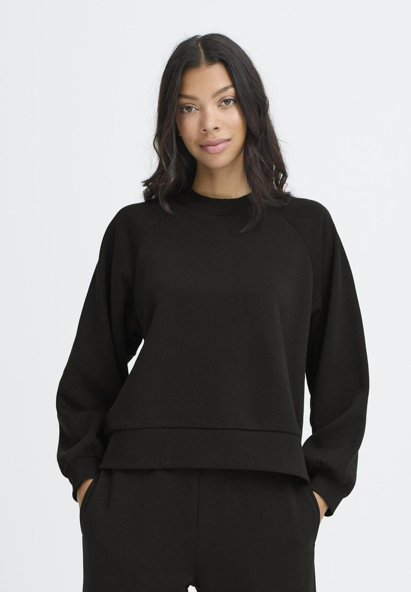 Melnā džemperī ar apaļu kakla izgriezumu, raglānu piedurknēm un brīvu piegriezumu. Iezīmēts ar apstrādātu apakšmalu un mīkstu, strukturētu audumu.