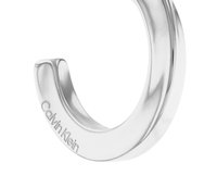 Bracelet jonc en métal argenté présentant un design lisse et courbé, avec l'inscription "Calvin Klein" gravée d'un côté. Fini poli, style minimaliste.