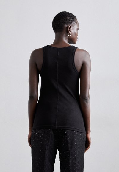 Fekete, ujjatlan trikó, tapadós fazonnal és sima textúrával. Hátul varrás található, és texturált fekete nadrággal párosítható.