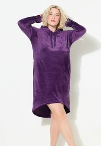 Violetti velour-huppari mekko, jossa on kaareva helma, pitkät hihat ja kiristysnauha hupussa. Edessä on hienovaraisia kimalteita.