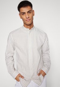 Lightweight, long-sleeve shirt featuring vertical beige and white stripes, a band collar, and button closures along the front.