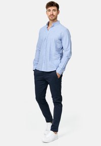 Chemise à manches longues bleu clair avec un col boutonné, associée à un pantalon marine et des baskets blanches. Tissu lisse avec une coupe décontractée.