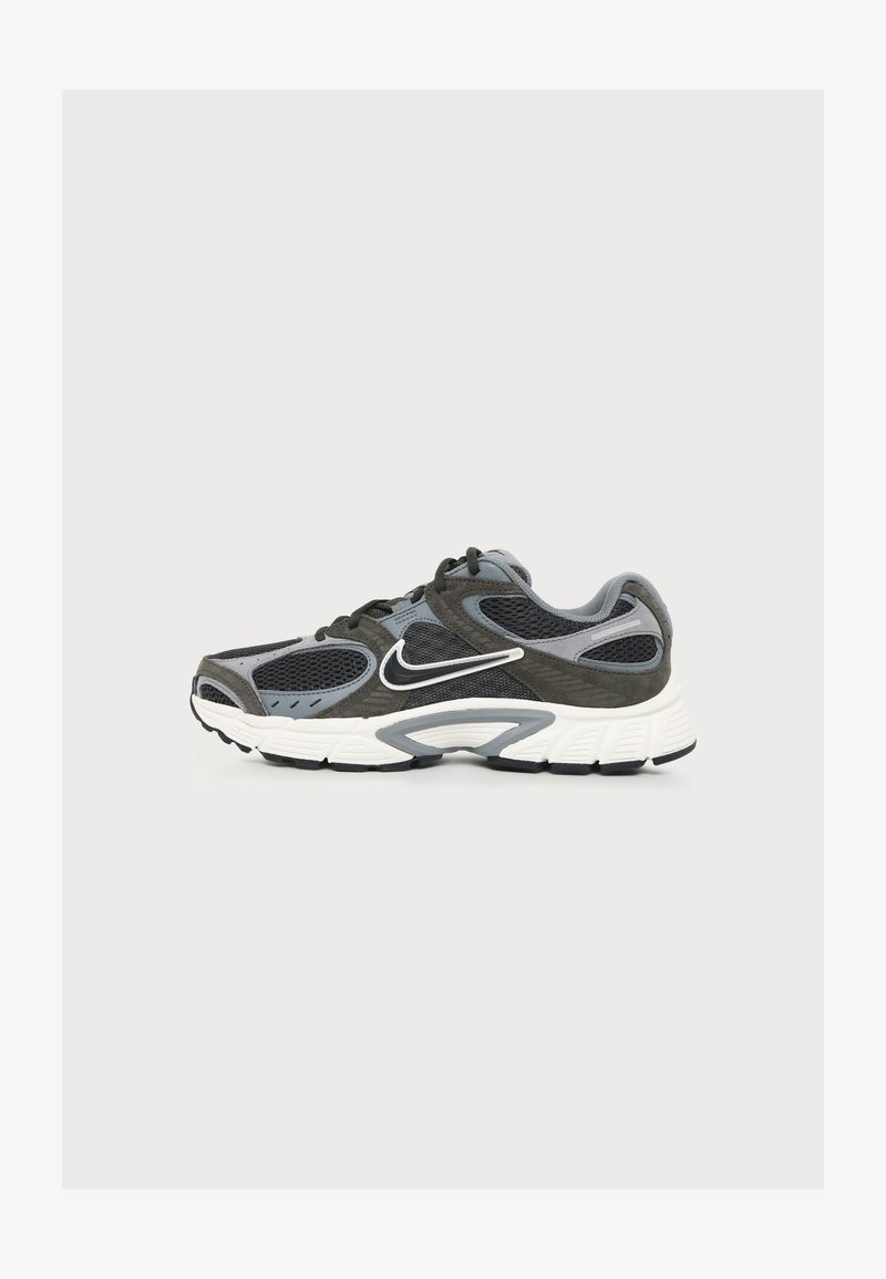 Γκρι και μαύρο αθλητικό παπούτσι Nike με λευκή σόλα και λογότυπο Swoosh, με τμήματα από δίχτυ και σουέντ, σε θέα από την εξωτερική πλευρά.